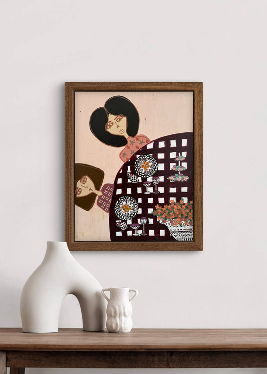 Framed artwork of two stylized figures on a wall above a wooden table with decorative vases.